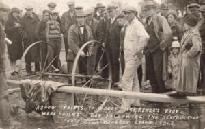A Group Of Men, Women And Children Stands Outdoors Around A Wagon As A Handwritten Caption And Arrow Indicate A Spot On The Ground.