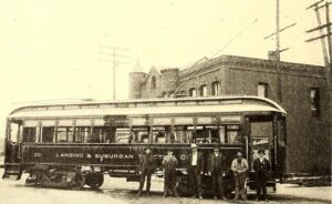 Black-And-White Photo Of Lansing &Amp; Suburban Traction Co. Streetcar No. 201 With Five Men Standing In Front Of It Beside A Large Brick Building And Utility Poles.