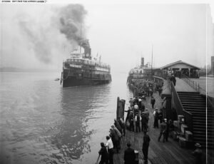 City Of Cleveland Iii - A Large Passenger Steamship Approaches A Pier Crowded With People While Smoke Rises From Its Stacks And Another Ship Sits At The Dock.