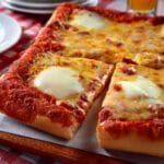 A Square Pizza With Cheese And Sauce On A Table