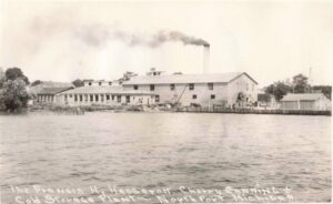 A Long Industrial Building Sits On The Waterfront With A Smokestack Releasing Dark Smoke, And Handwritten Captioning Identifies It As The Francis H. Haserot Cherry Canning And Cold Storage Plant In Northport, Michigan.