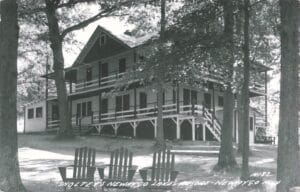 Black-And-White Photo Of A Large Lodge-Style Building With Wraparound Porches And Lawn Chairs In The Foreground, Labeled “Sholtey’s Newaygo Lakes Resort — Newaygo, Mich.”