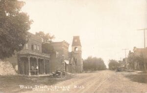 Sepia-Toned Photo Of A Wide Dirt Street Lined With Two-Story Buildings And A Few Early Cars, Labeled “Main Street Leonard Mich.”