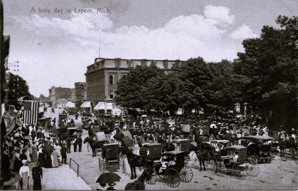 A Crowd Of People In A Street With Horse Carriages