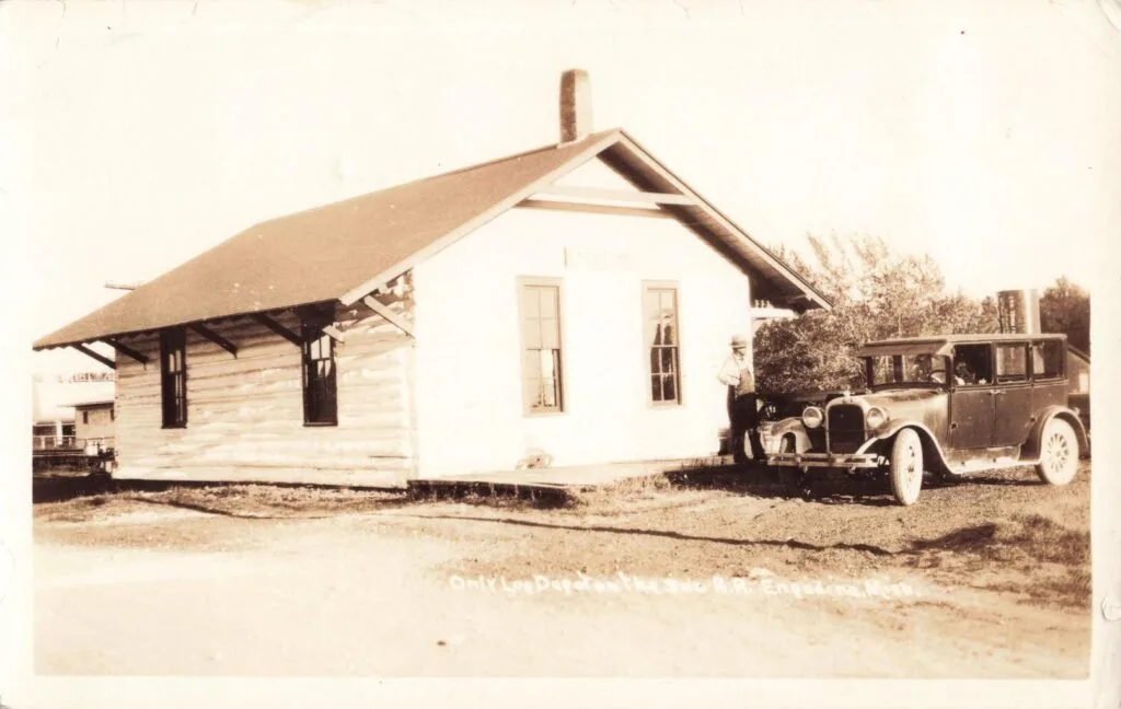 A Man Standing Next To A Car In Front Of A Depot