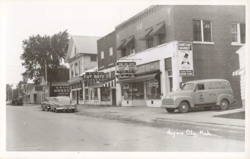 A Black And White Photo Of A Street With Shops And Cars