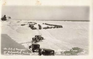 Black-And-White Photo Of Many Covered Vintage Cars Parked In Rows On A Snowy, Frozen Lake Superior Shoreline With The Open Horizon In The Distance.