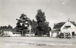 A Roadside Grocery, Motel And Post Office In Au Train, Michigan, Sits Beside A Texaco Sign And Two Vintage Gas Pumps, With Cars Parked Out Front.