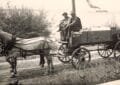 Black-And-White Photo Of A Horse Harnessed To A Wooden Wagon Labeled “Ice Wagon,” With Two Men Seated On The Front Bench On A Dirt Road Near The Shoreline And A Steamer In The Distance.