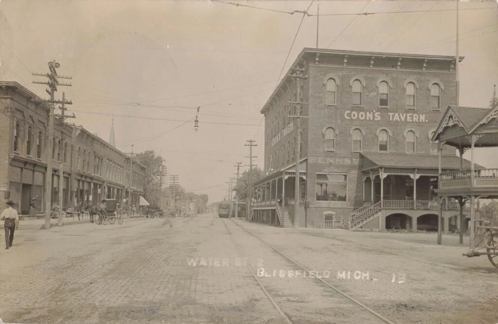 Coon’s Tavern Landmark Building On A Wide Downtown Street With Rail Tracks Visible.