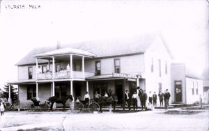 Sepia Street Scene Of Howard Avenue In Croswell With Multi-Story Brick Buildings, Storefront Awnings, Utility Poles, And A Horse-Drawn Buggy.