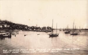 Sepia-Toned Harbor Scene With Many Sailboats On The Water And A Shoreline Neighborhood With A Church Steeple In The Distance.