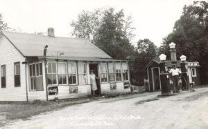 Historic Bryers Service Station In Bitely, Michigan, With Three Gasoline Pumps, Two People, A Small Roadside Building And Coca-Cola And 7-Up Advertising Signs.